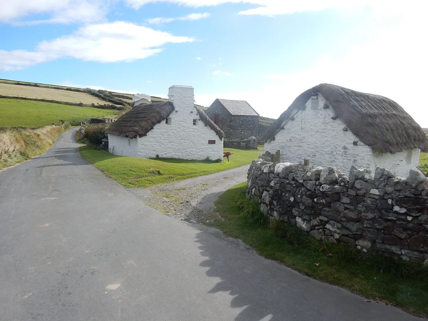 Whitewashed thatched cottages beside a narrow lane and stone walls in Cregneash.